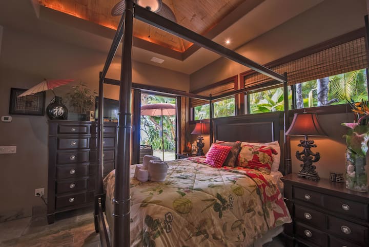 Hosťovský apartmán s manželskou posteľou v štýle Bali, televízor, posúvač s výhľadom na oceán a bambusový strop.