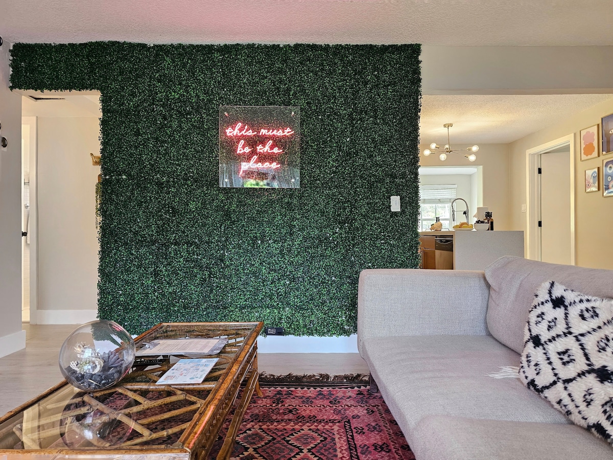 A living area with a lush green living wall creates a unique backdrop. A light-colored sofa is positioned in front, accompanied by a decorative coffee table featuring a round glass centerpiece. The flooring is adorned with an intricate rug, enhancing the space's character.