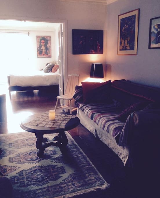 Cozy living room with couch, chaise lounge, TV. View into second bedroom which is separated by French doors.