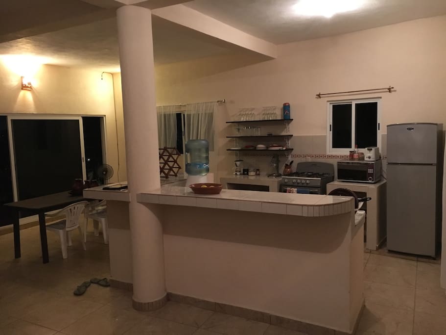 Open kitchen with refrigerator, gas stove, microwave, coffee machine, orange press, pots and pans, dishes and cutlery