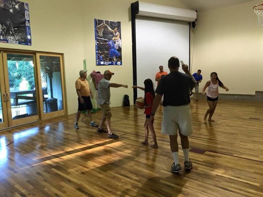 These families are enjoying a fun game of H-O-R-S-E in the in-door basketball area. The large windows look out to the backyard and sitting areas. The size of the court traces a few feet outside of the 3-point line.
