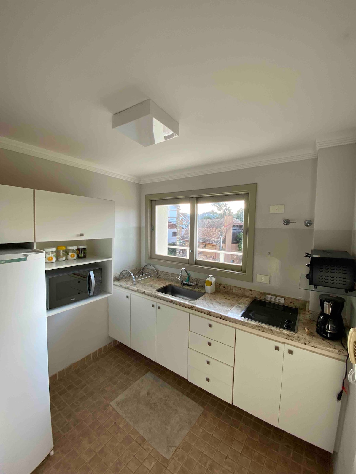 A compact kitchen is equipped with essential appliances, including a refrigerator, microwave, and coffee maker. Light-colored cabinets and granite countertops are complemented by a window offering natural light. The layout allows for efficient use of space, including a sink and cooking area.