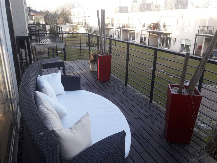 Hermosa terraza con vista al gran parque descansando en un comodo sillon con almohadones.