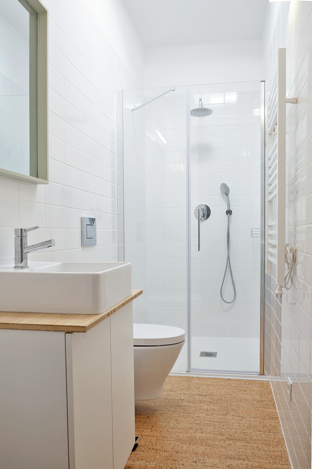 A modern bathroom is depicted, featuring a walk-in shower enclosed by clear glass. A sleek sink sits atop a wooden vanity, while a toilet is positioned nearby. Light-colored tiles adorn the walls, complemented by a large mirror that reflects natural light.