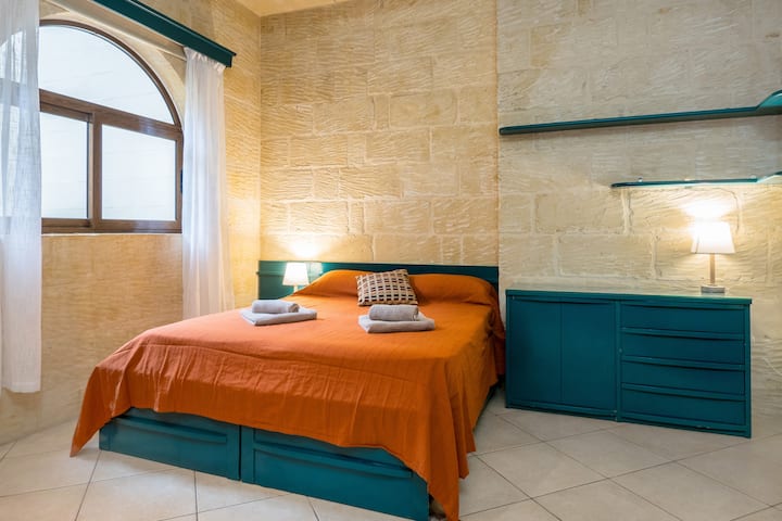 غرفة نوم مزدوجة بحمام خاص وشرفة. شواحن جدارية ومرآة طويلة ومروحة سقف.