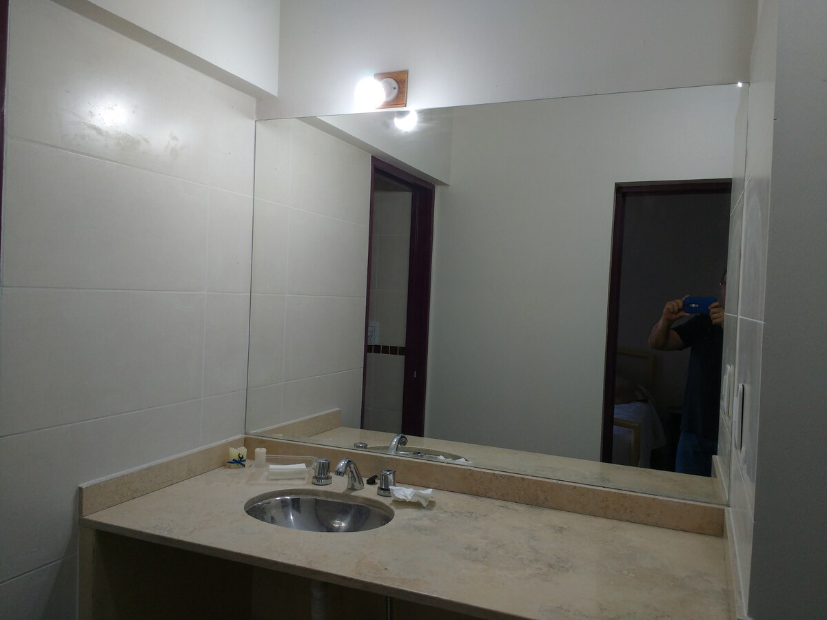 A modern bathroom is displayed, featuring a spacious dual sink vanity with a polished stone countertop. A large mirror is positioned above the sinks, reflecting soft lighting. Neutral-colored tiles surround the area, contributing to a clean and minimalist design.