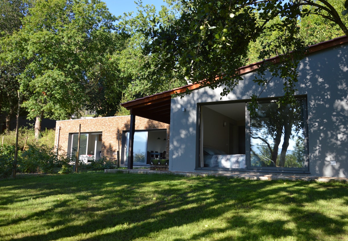 The exterior of the casa da Lavanda showcases a modern design, featuring large windows that allow natural light to fill the interior. A spacious lawn area extends around the house, surrounded by lush trees, providing a peaceful and private setting.