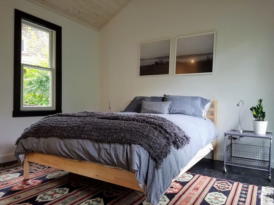 Cozy queen bed wrapped in a down comforter, with original art, live plant, on a gorgeous wool kilim.
