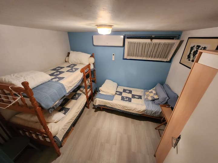 ห้องนอนที่ 2 พร้อมเครื่องปรับอากาศติดผนังเตียงสองชั้นและเตียงเดี่ยวที่ด้านหลังของที่พักชั้นบน  เตียงเด็กอ่อนอยู่ใต้เตียงสองชั้น