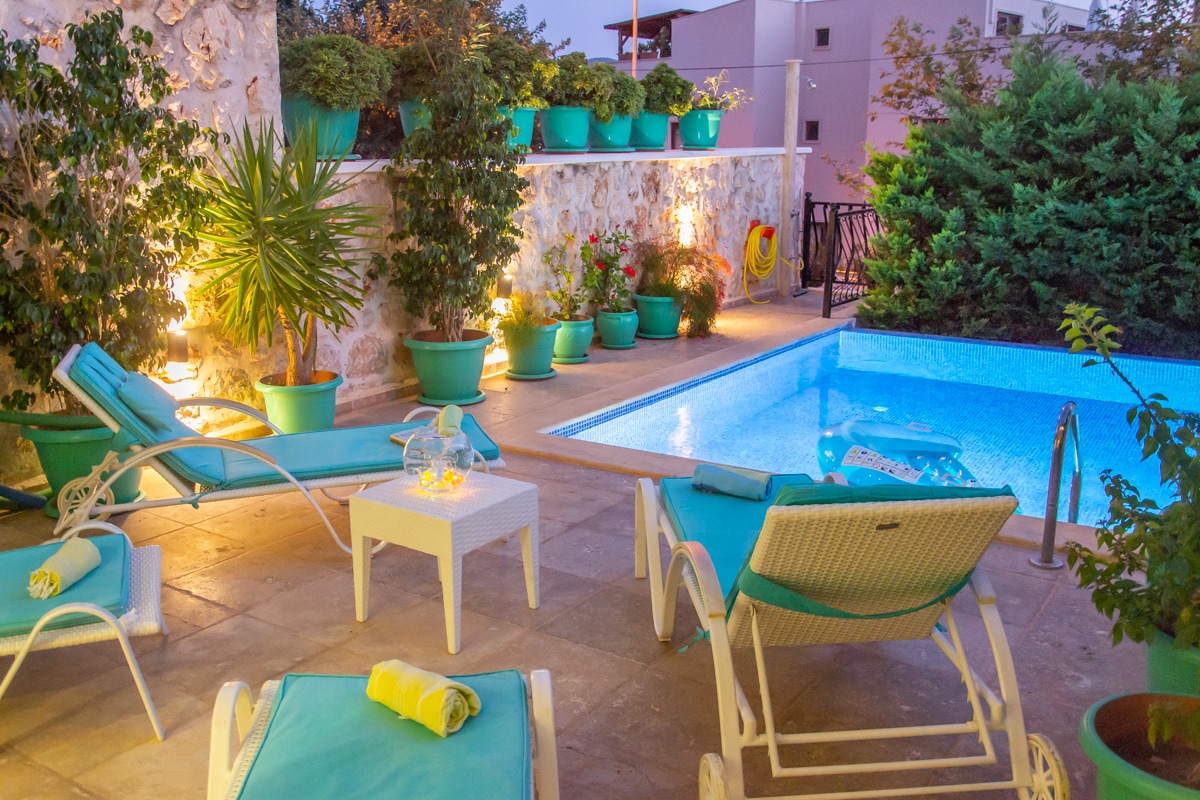 A private outdoor space features a plunge pool surrounded by well-maintained greenery and colorful planters. Comfortable sun loungers are arranged near a small table, providing a serene area for relaxation. Soft lighting enhances the ambiance during the evening hours.