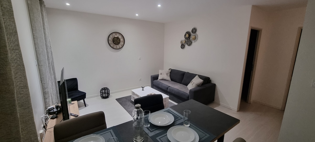 A modern living area features a neutral color palette with a comfortable gray sofa and two armchairs. A coffee table sits at the center, with decorative items adorning the walls. Soft lighting illuminates the space, enhancing its welcoming ambiance.
