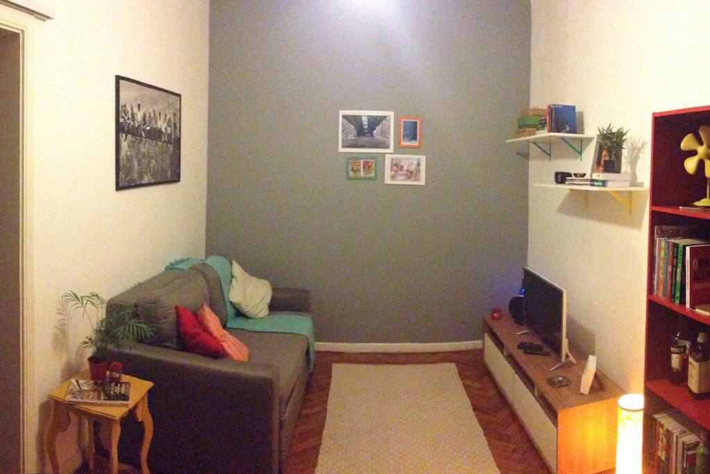 Visão maior da sala com o sofá cama à esquerda, ele vira uma cama de casal.