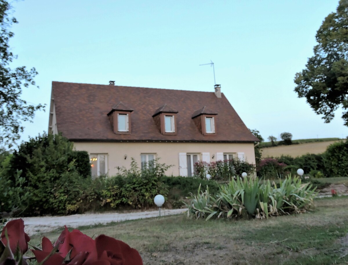 The charming périgourdine house is surrounded by lush greenery and garden plants. Its sloped roof features three dormer windows, and the exterior is complemented by outdoor lighting along the pathway leading to the entrance.