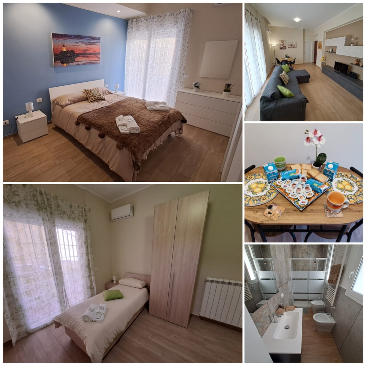 A comfortable bedroom features a spacious bed, accented by a brown throw and neatly arranged white towels. Large windows allow natural light, and a painting adds a touch of color to the blue wall. A cozy seating area and modern decor create a welcoming ambiance.