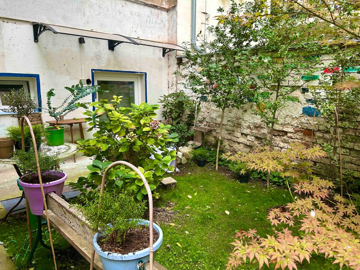 A small garden space is visible, featuring potted plants in vibrant containers. The garden is bordered by a textured stone wall, providing a natural backdrop. Lush greenery and a wooden bench create a serene environment, inviting moments of relaxation in an intimate outdoor setting.