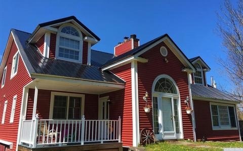 The exterior of the converted barn features a vibrant red facade with white trim. Large windows allow natural light to fill the space, while the front porch is adorned with seating. A classic archway stands prominently at the entrance, enhancing the home's character.