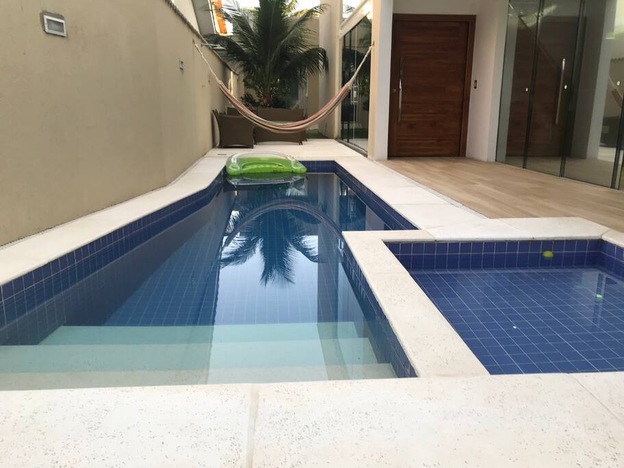 Visão das duas piscinas (adultos e crianças) com sofás e mesa ao fundo.