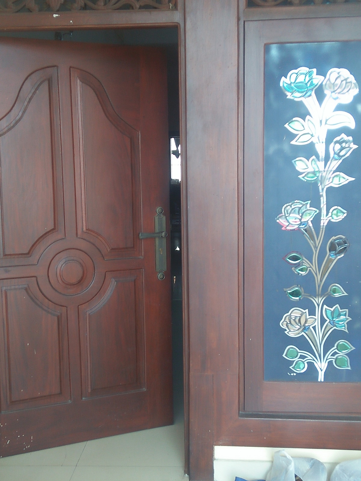 A wooden door with an intricate design is partially open, revealing a glimpse into the interior. Beside the door, a decorative panel features colorful floral elements against a dark background, adding a touch of elegance to the entrance.
