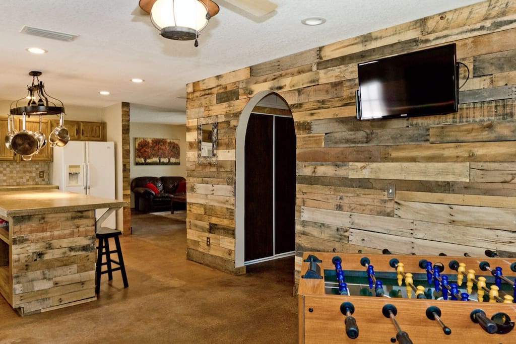 Pallet wood walls with a large island in the kitchen and a foosball table and flat screen tv