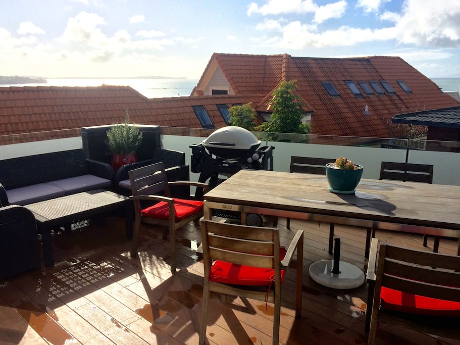Large first floor deck, with ocean views, BBQ, dining table and sofa area.