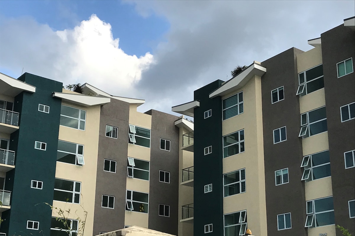The image presents a modern condominium building featuring multiple stories with distinct color patterns. Large windows offer ample natural light, while balconies extend from the upper floors. The rooflines are elegantly designed, contributing to the contemporary aesthetic of the architecture.