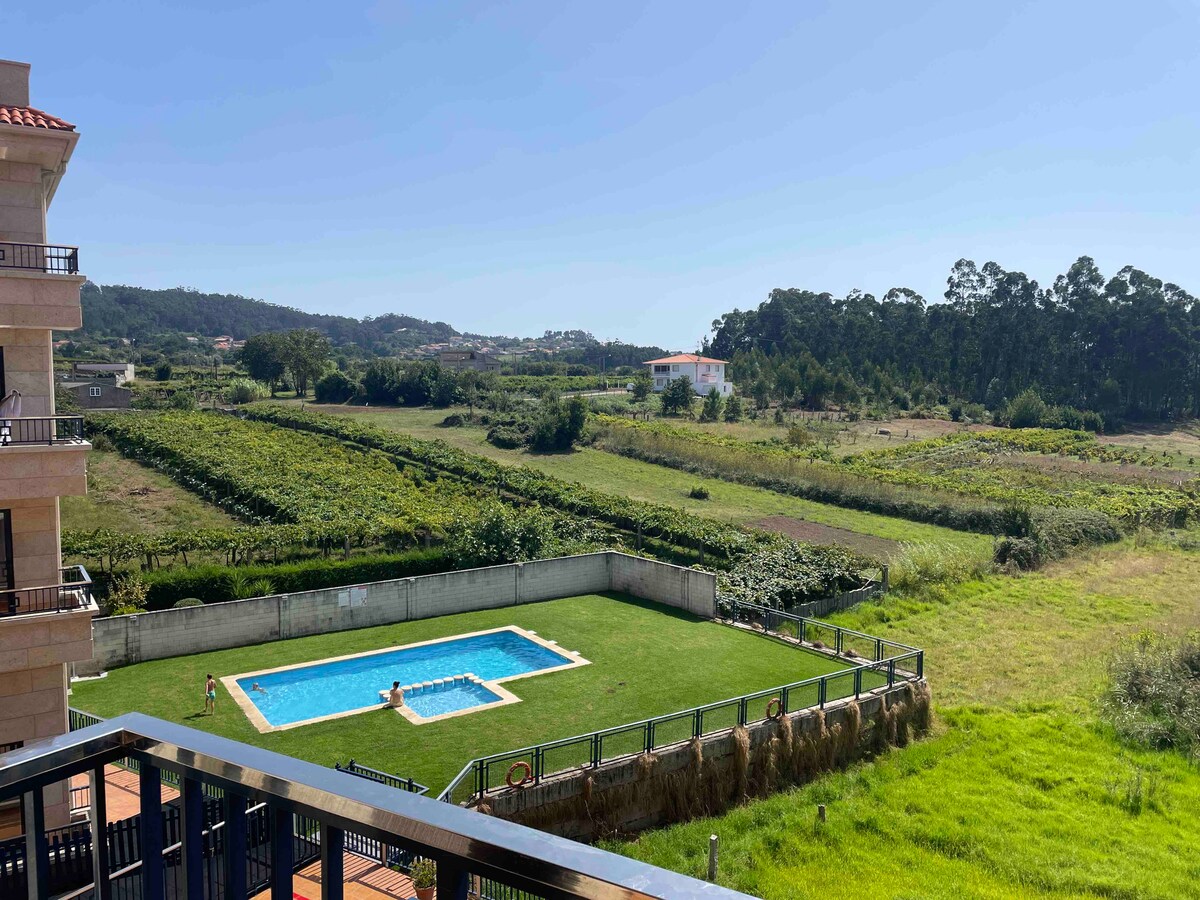 A serene view features a well-maintained outdoor swimming pool surrounded by a grassy area. Lush green fields and distant trees provide a natural backdrop, contributing to the peaceful setting. The image captures clear blue skies and a sense of openness.