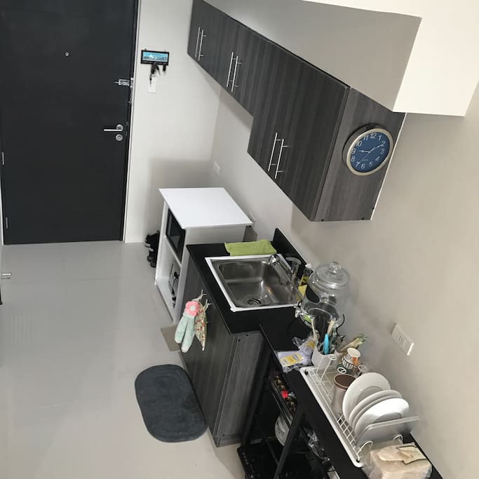 Kitchen with microwave, oven, induction stove, rice cooker, water heater, personal fridge. Also with plates, mugs, utensils, and water dispenser