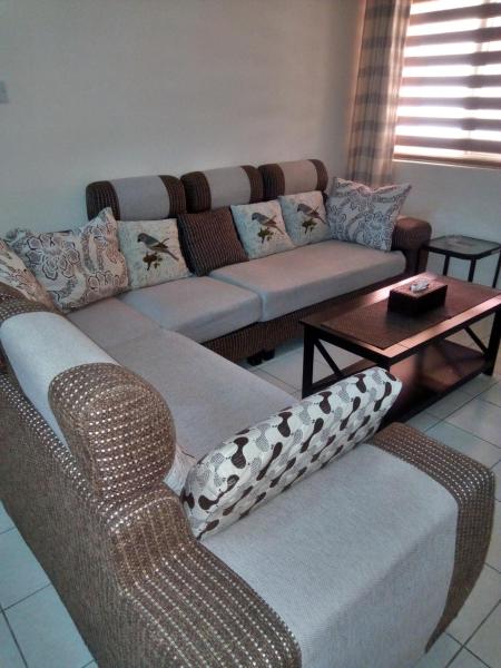 A cozy living area is presented with a spacious sectional sofa featuring muted tones and decorative cushions. A low coffee table is positioned in front, creating a functional gathering space, while natural light filters through the window adorned with striped blinds.