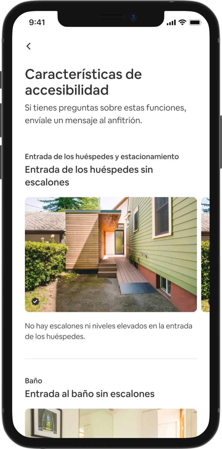 Un celular muestra los detalles de un alojamiento de Airbnb. El encabezado dice “Prestaciones de accesibilidad” y aparecen las prestaciones agrupadas por zonas, como “Entrada de los huéspedes y estacionamiento” y “Baño”. Debajo de “Entrada de los huéspedes y estacionamiento” aparece el título “Entrada sin escalones” y la descripción “No hay escalones ni bordes elevados en la entrada de los huéspedes”. Debajo aparecen varias diapositivas con fotos de esta pretación en el alojamiento, empezando con una rampa para sillas de ruedas.