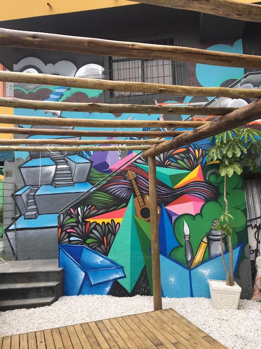 Área externa privativa inteiramente reformada. Ambiente descolado e super agradável. Possui deck rústico com pergolado, iluminação LED e tomada externa, parede toda grafitada por artista local, variedade de plantas no jardim, churrasqueira de latão, pia com bancada e uma rede de balanço de descanso.
