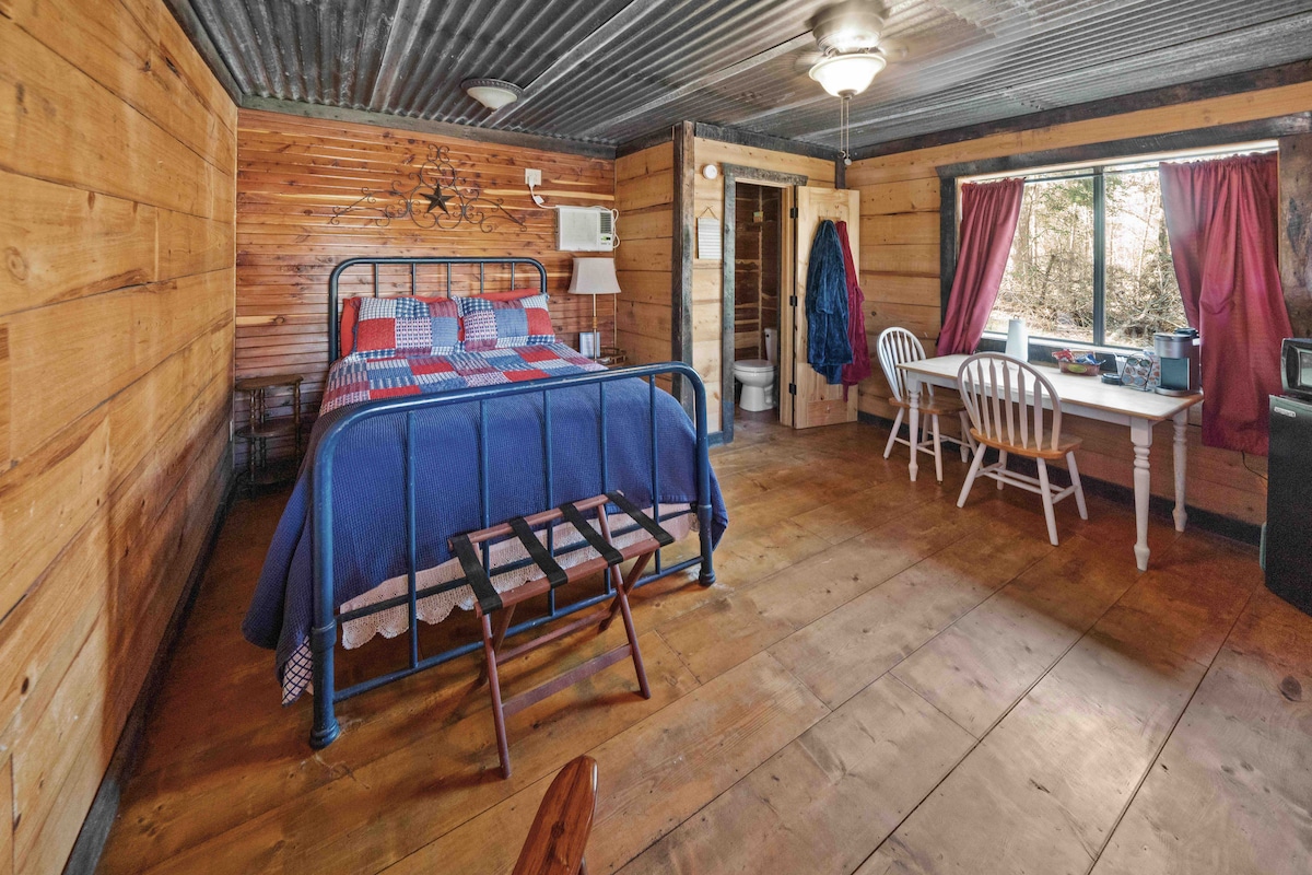 Efficiency style room with half bath, mini fridge, microwave, table, two chairs, rocking chair, and full size bed. 