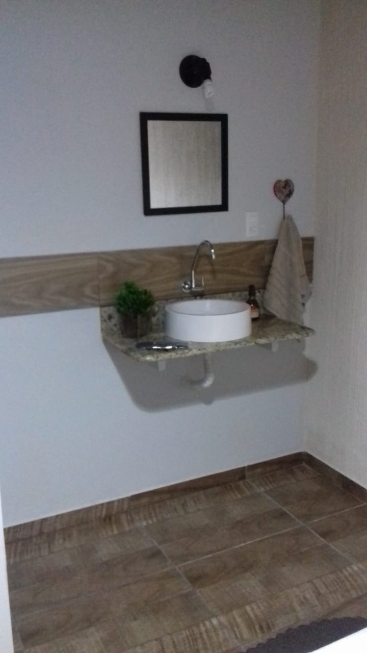 The bathroom features a modern sink mounted on a granite countertop, accompanied by a mirror above. A small plant adds a touch of greenery, while a towel hangs nearby. The warm-toned tiles cover the floor, contributing to a clean and functional space.