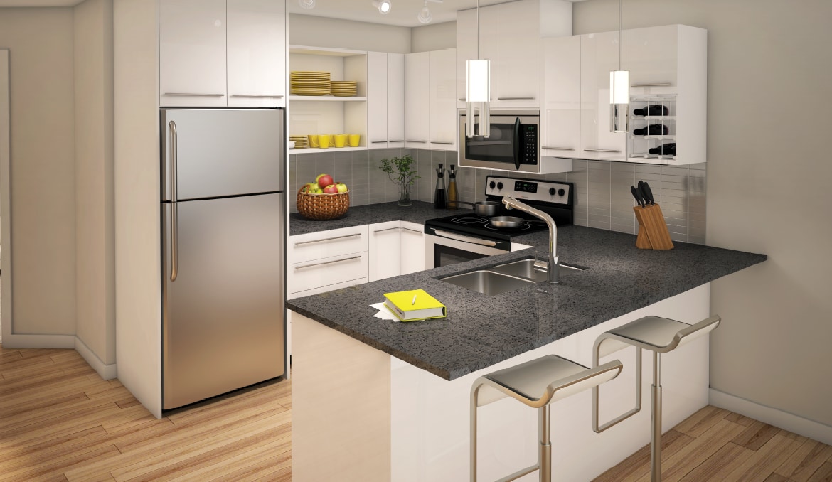 A modern kitchen is presented with sleek white cabinetry and a spacious countertop. Stainless steel appliances, including a refrigerator and microwave, complement the design. A bowl of fruit is displayed on the countertop, while pendant lights provide illumination over the bar seating.