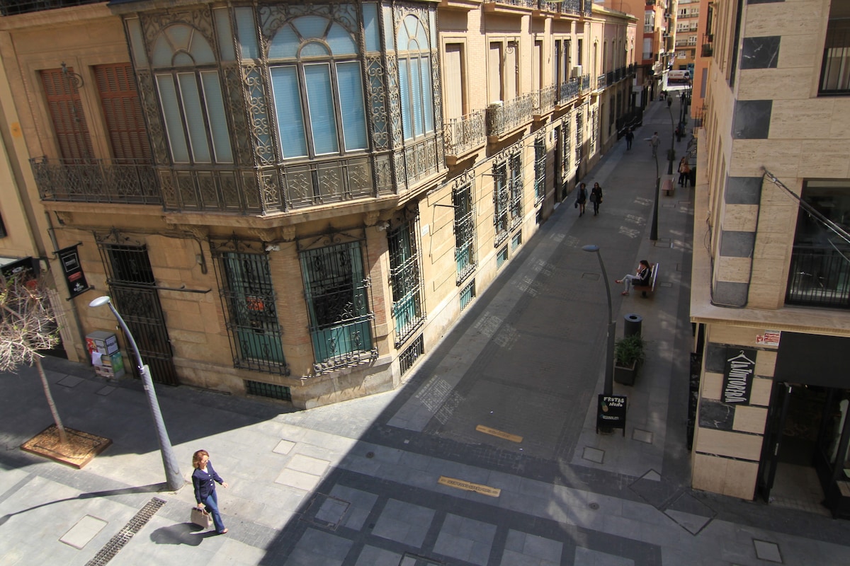 A pedestrian street is depicted, featuring attractive architectural details on the surrounding buildings. Streetlamps line the pathway, and a few pedestrians can be seen walking. The area appears spacious and well-maintained, contributing to a serene urban atmosphere.