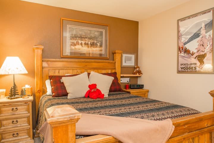 מיטת קווין סייז בחדר האורחים עם הרבה כריות ושמיכות, מקושטות בפוסטרים של סקי ובעיצוב הרים. זה יהיה מקום הבילוי שלכם, ויכלול טלוויזיה חכמה, חדר ארונות גדול כדי לחפור במזוודה ושולחן.