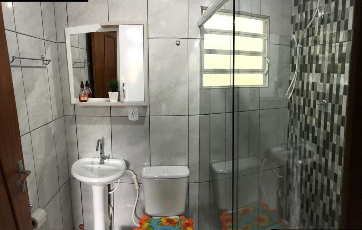 The bathroom features modern tile work and includes a glass-enclosed shower with a hot water system. A pedestal sink and toilet are present, accompanied by a small window for natural light. A vibrant mat adds a touch of color to the floor.