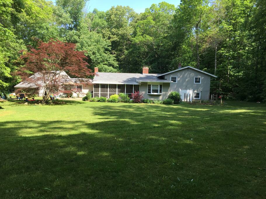 Large, spacious, private backyard, surrounded by woods, featuring outdoor shower, fire pit, stone patio, and vegetable garden.
