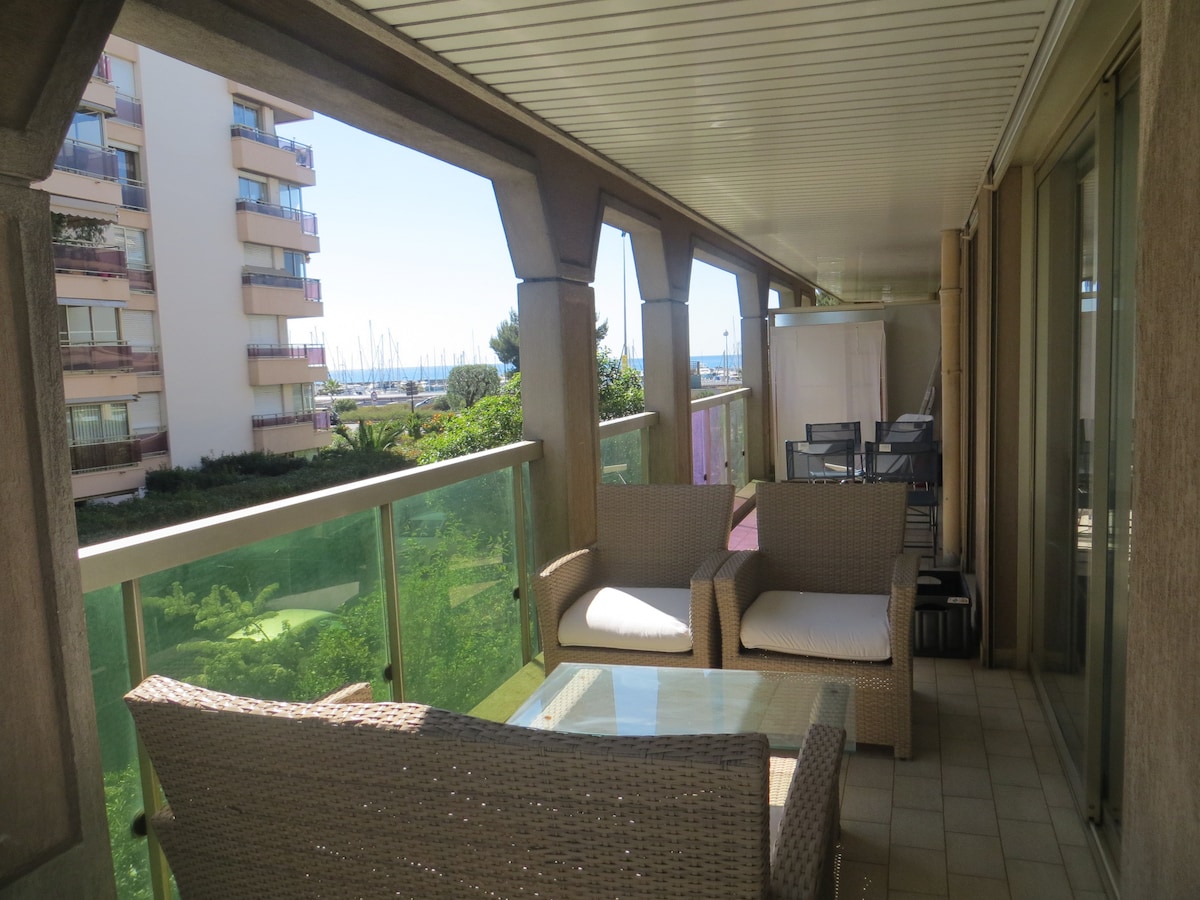 A spacious terrace is shown, featuring comfortable wicker seating and a glass coffee table. Views of greenery and the sea can be seen in the background. The terrace offers a relaxing atmosphere with ample space for outdoor enjoyment.