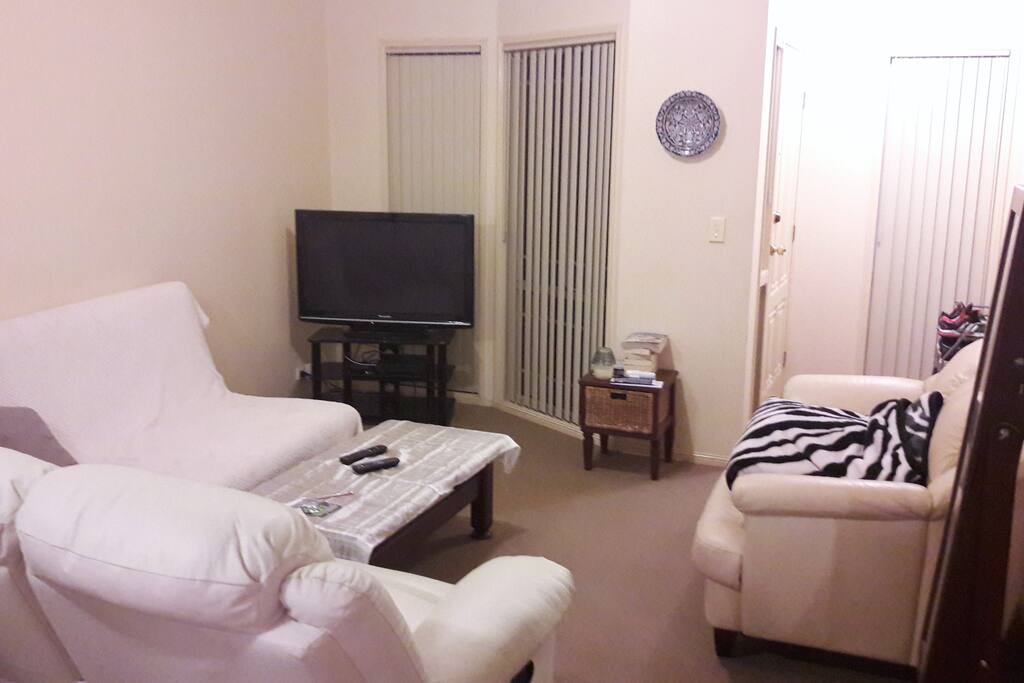 Modern and spacious living room downstairs with air conditioner. Comfortable seating and high ceilings. Plasma TV.