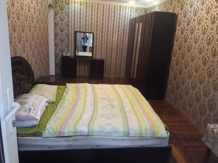 Bedroom with king size bed, wardrobe, mirror table, two (bed) side drawers and small table in the corner