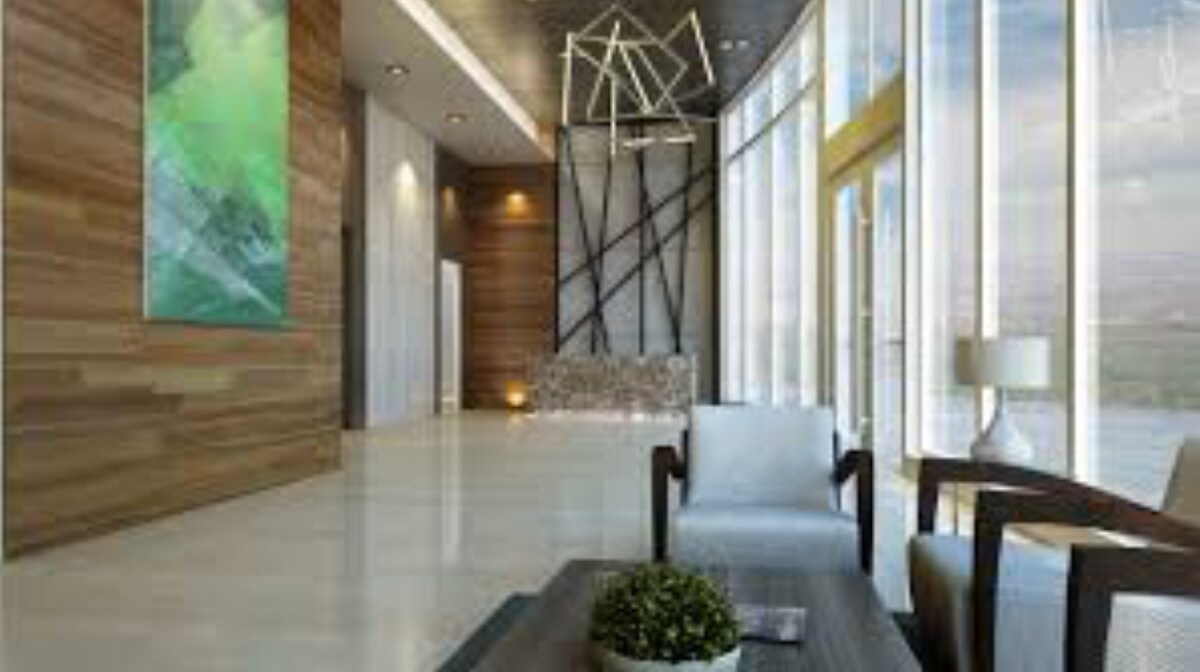 A modern lobby area is characterized by sleek lines and large windows, allowing for ample natural light. A minimalist seating arrangement features two white chairs and a dark coffee table adorned with a small plant. A vibrant piece of art adds a splash of color to the wooden wall.