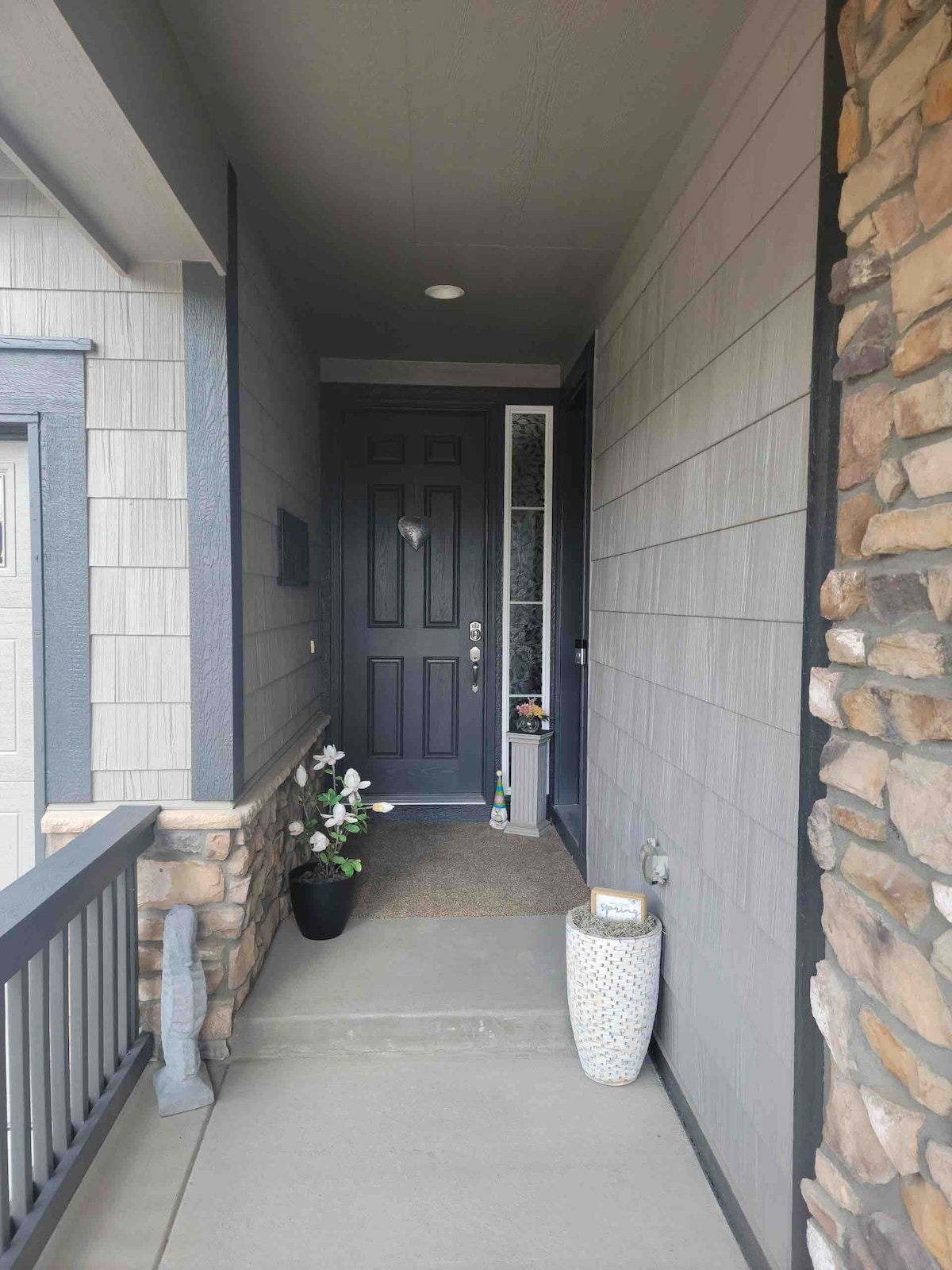 A welcoming entrance is featured, showcasing a dark front door set against a light-colored exterior. A small stone accent adds texture, while a potted plant and decorative vase enhance the space. The pathway is clear, leading to the door.
