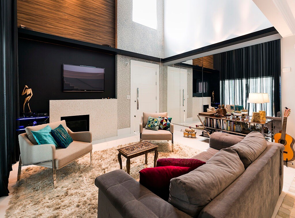 A spacious living area showcases a comfortable sectional sofa paired with two accent chairs. A textured rug covers the floor, while a sleek entertainment unit is positioned against the wall. Soft lighting creates a cozy ambiance, complemented by decorative elements and artwork.