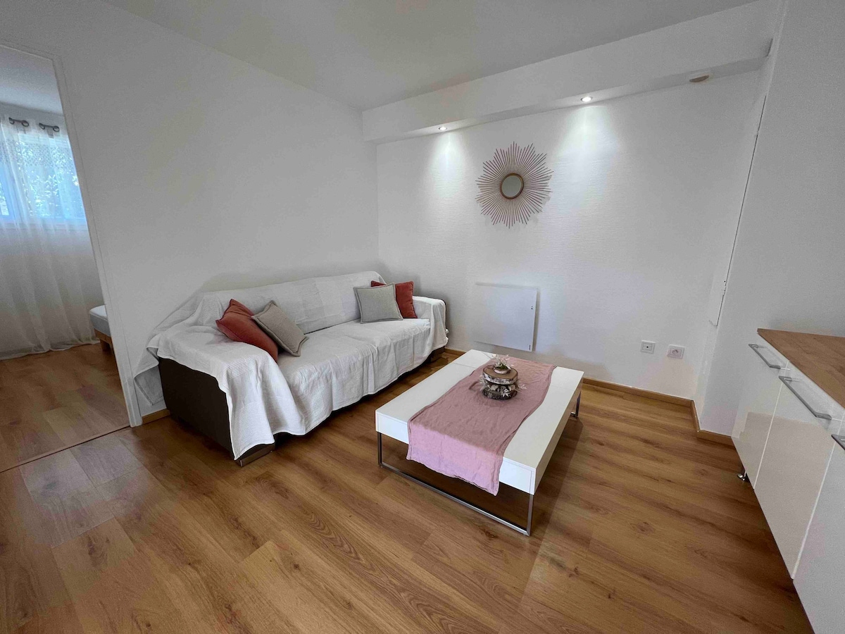 A bright living area features a spacious sectional sofa draped with a light cover, complemented by decorative pillows. A sleek coffee table holds a decorative bowl, while soft lighting highlights the white walls and light wooden flooring.