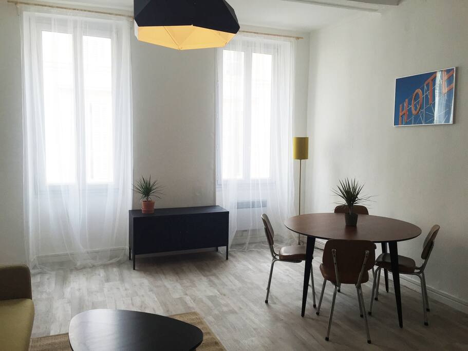 Salon clair avec clic clac pour une personne, table basse et vraie table pour les repas avec deux fenêtres