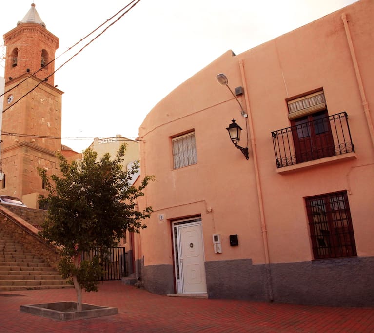 Fachada y entrada principal, se ve la iglesia del pueblo que está justo al lado, separada por una escalera.
