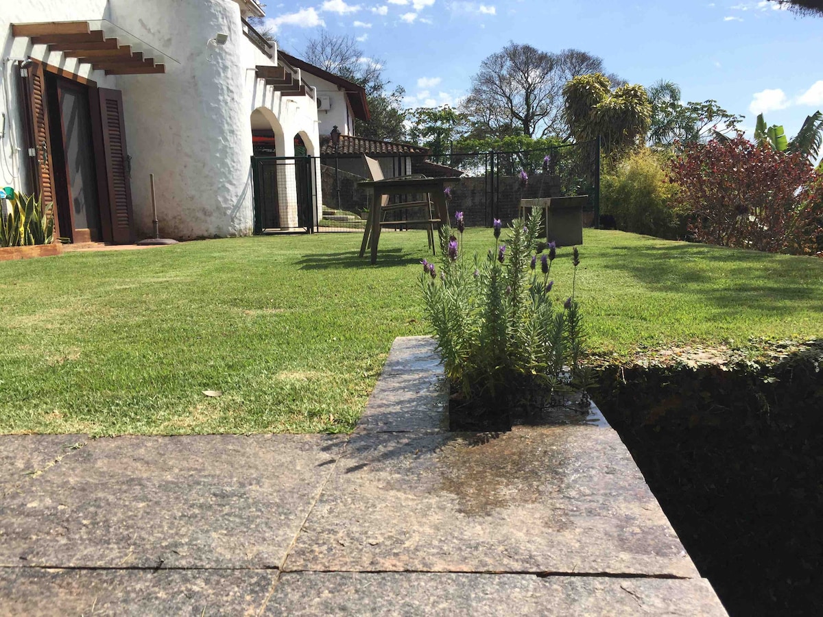 A spacious garden area is seen with well-maintained grass and a few lavender plants near a stone pathway. A wooden table and chairs are positioned on the grass, providing a serene spot to enjoy the outdoors. Lush greenery surrounds the property.
