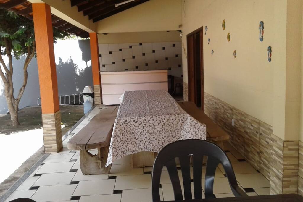 Varanda dos fundos da casa com mesa grande e bancos de madeira
