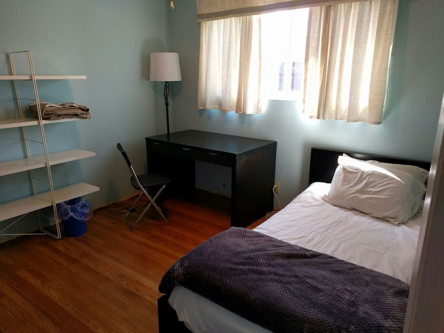 Cozy bedroom with twin bed and wooden desk. Ample shelf/closet space. Light fixtures equipped with ceiling fans.