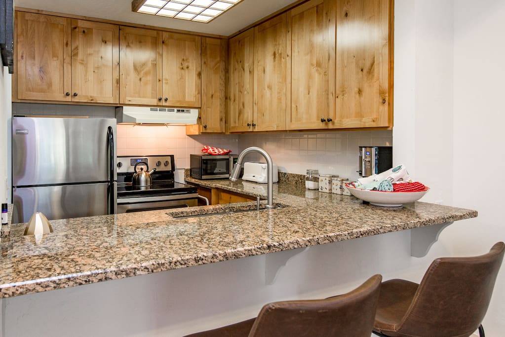 The kitchen includes stainless steel appliances and a breakfast bar with two stools.